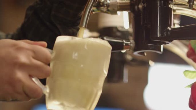 4k将冰镇啤酒倒入玻璃杯中。酒保在酒吧里倒精酿啤酒。啤酒酿造大师的手从小桶中倒入淡淡的生啤酒泡沫。烈