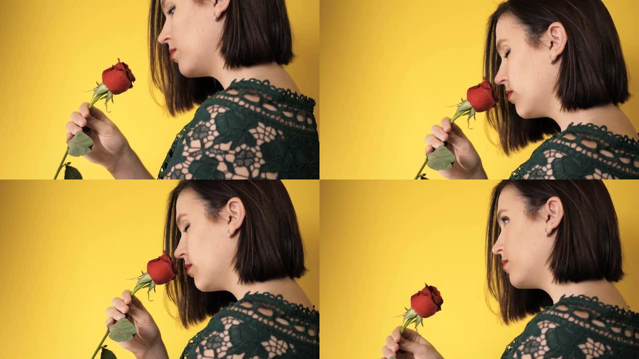 右手拿着红玫瑰的女孩若有所思地嗅着黄色背景上美丽的花朵。情人节，2月14日，生日，周年纪念日，第一次