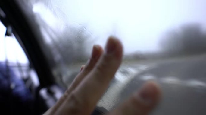 男性的手擦拭一扇雾蒙蒙的窗户。车里的乘客擦玻璃。