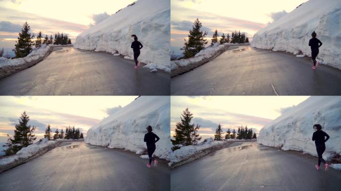 自信的女慢跑者在柏油马路上奔跑映衬山里的金色夕阳