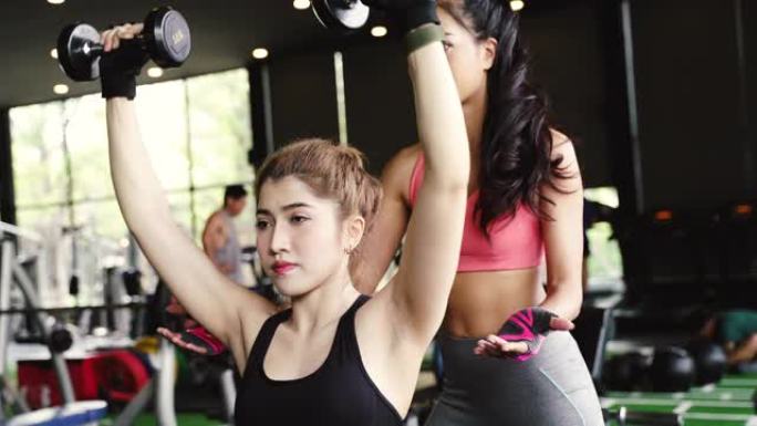 亚洲私人教练指导一名健美女子在健身馆用哑铃进行举重运动。