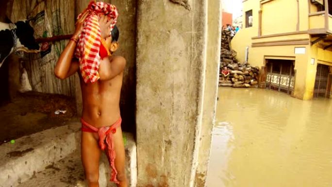 小印度男孩用格子红色材料擦干湿的身体脏水洪水圣河恒河楼梯上的灰木堆火化地点smashan洪水建筑物瓦