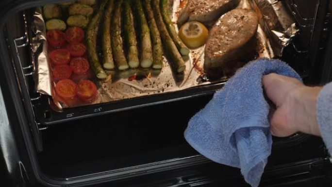 烤三文鱼牛排和蔬菜的特写镜头。在电烤箱中准备的煮熟的鱼和西红柿。健康饮食。女人从烤箱里拿出晚餐。家庭