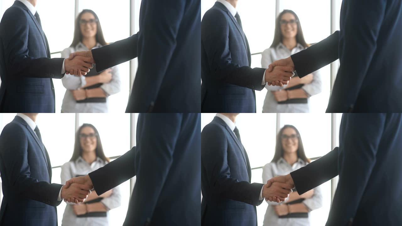 两个商业伙伴见面时握手。迷人的女秘书在后台