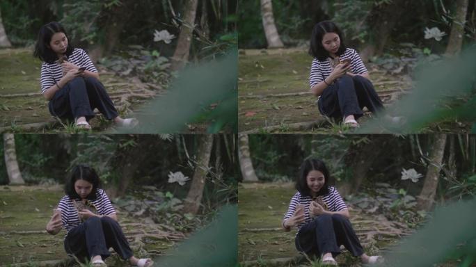 亚洲女孩在森林里用智能手机和可爱的猫。