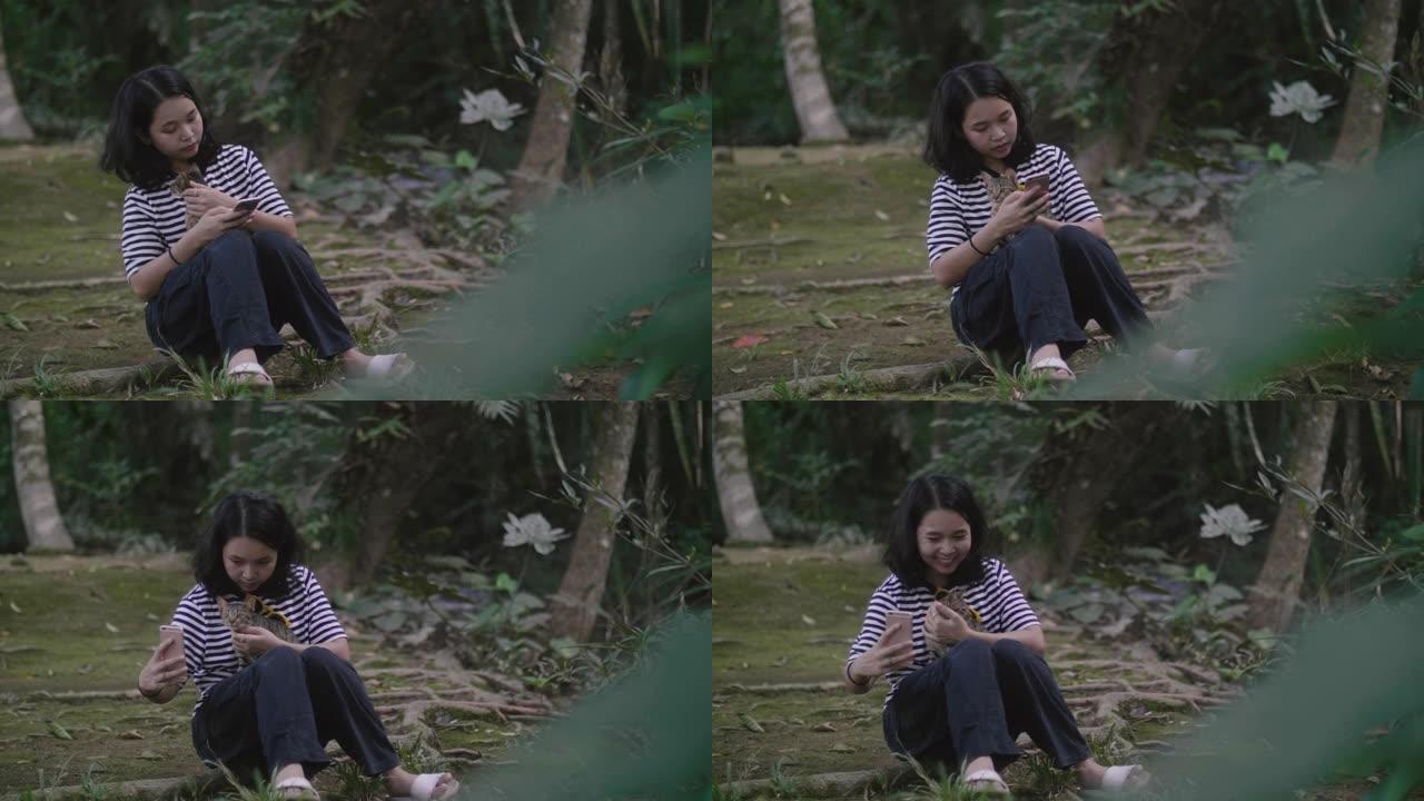 亚洲女孩在森林里用智能手机和可爱的猫。