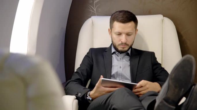 年轻自信的律师商人正在使用坐在企业家飞机内部的平板电脑