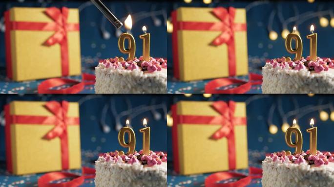 白色生日蛋糕编号91点灯燃烧的金色蜡烛，带灯的蓝色背景和用红丝带绑起来的礼物黄色盒子。特写