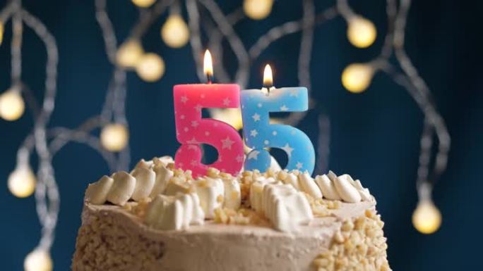 蓝色背景上有55号粉色蜡烛的生日蛋糕。蜡烛吹灭了。慢动作和特写视图