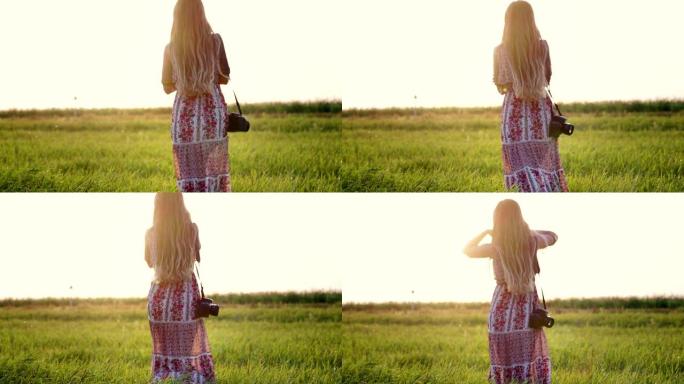 年轻的嬉皮士女人，肩上扛着相机，在日落时穿过田野