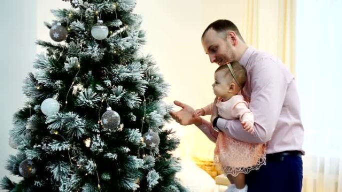 父亲带着宝贝女儿在圣诞树附近的家中。家庭和父亲身份