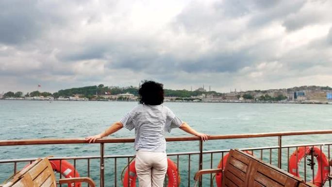 土耳其年轻女子在博斯普鲁斯海峡享受乘船游览，背景是伊斯坦布尔阿亚索非亚