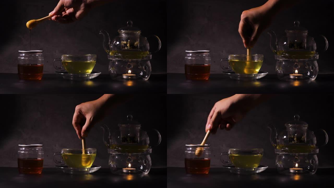 男人的手拿着蜂蜜棒，滴入厨房茶杯中的热绿茶中。经典茶壶由玻璃和蜡烛烧开水制成。热饮和茶时间概念。