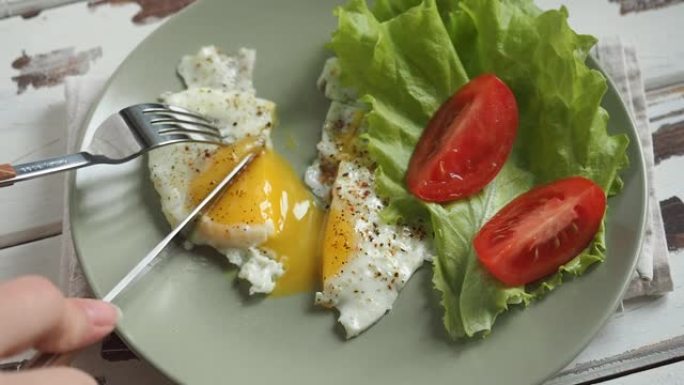 女人在盘子里吃早餐煎鸡蛋番茄和生菜。