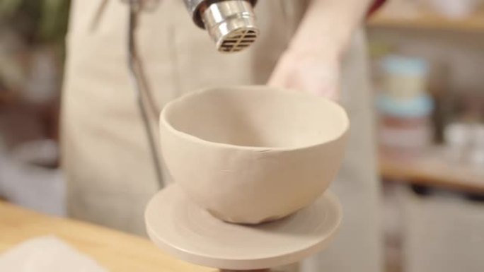 女陶工用热风枪干燥成品粘土碗的手