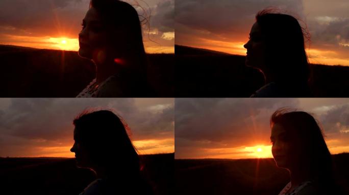 长发飘逸的女孩的轮廓站在田野的夕阳下。