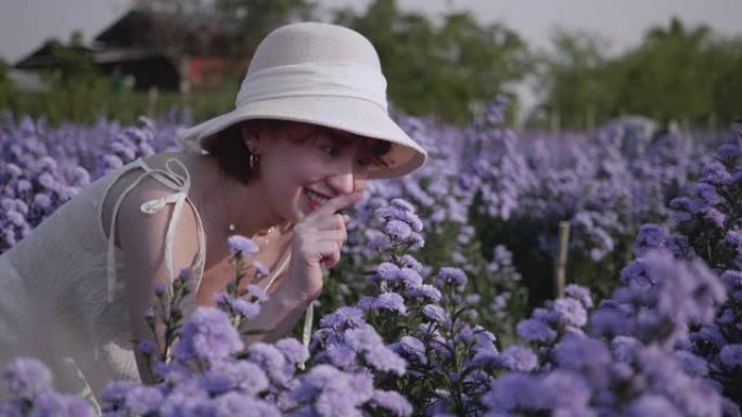 一个年轻的女人在阳光明媚的日子里轻轻地手里拿着鲜花，闻到紫色的花朵。慢动作