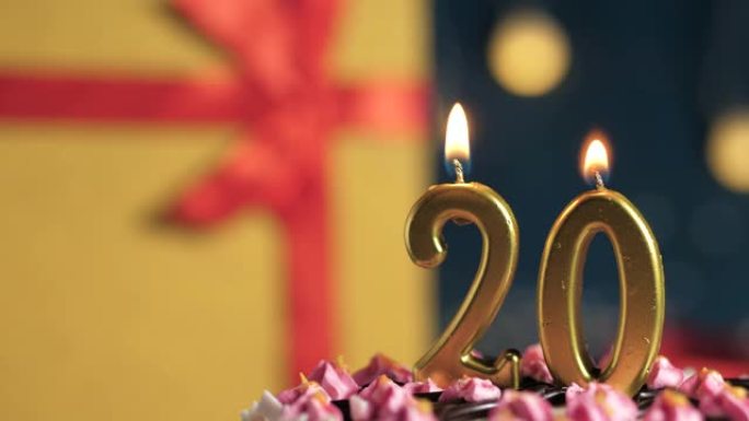 生日蛋糕20号点火器燃烧的金色蜡烛，蓝色背景礼物黄色盒子用红丝带绑起来。特写和慢动作