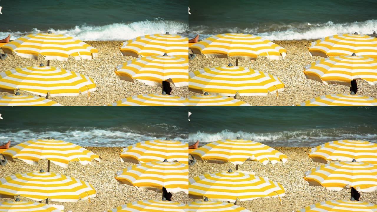 在多风的夏日，黄色和白色条纹的雨伞在鹅卵石海滩上打开
