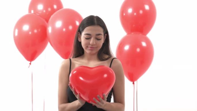 浪漫的女人，梦幻般的样子拥抱着心形的红色气球。站在一堆红色圆形气球附近的女人