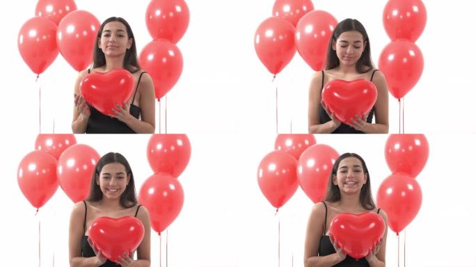 浪漫的女人，梦幻般的样子拥抱着心形的红色气球。站在一堆红色圆形气球附近的女人