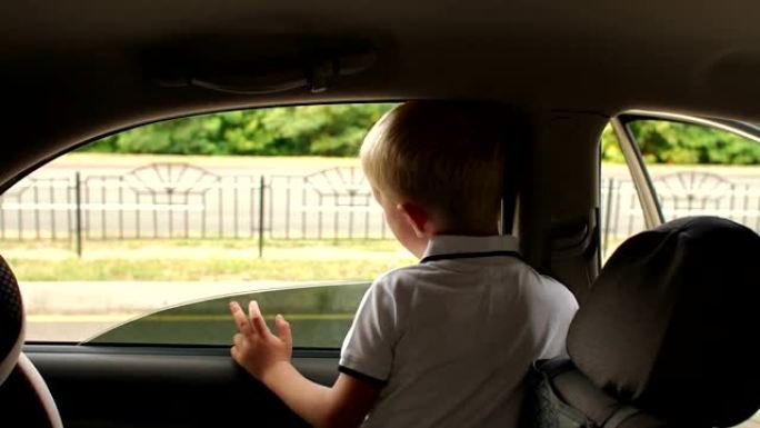 小男孩坐在汽车的后座上，他看着车窗外。