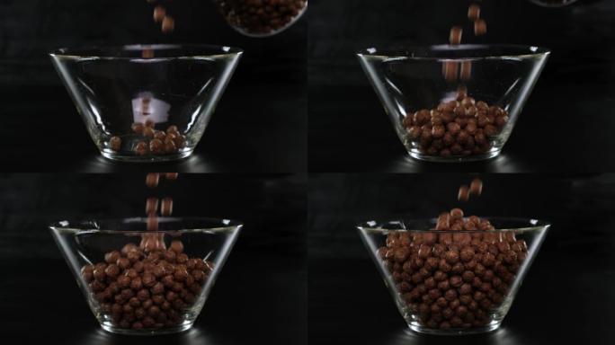 巧克力麦片球落在黑色背景上的透明方形碗中。
