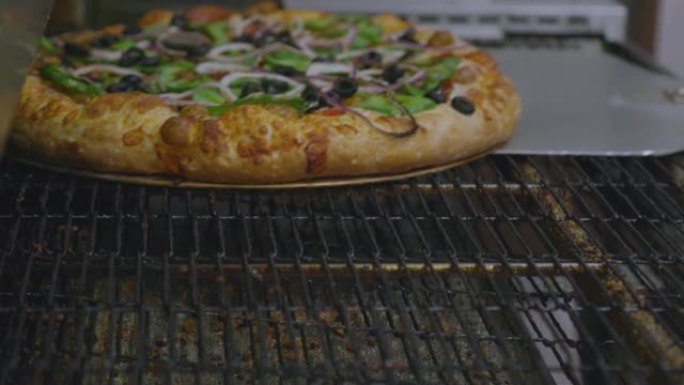 蔬菜披萨在传送带披萨烤箱上烘烤，餐厅厨房配有披萨皮