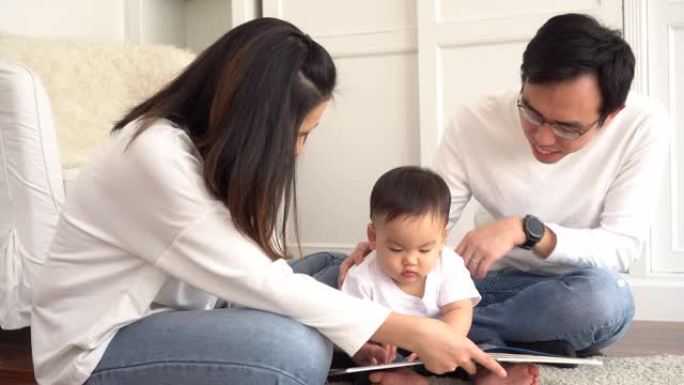 快乐的现代亚洲父母和可爱的小男孩坐在地板上，一边在家里一起享受时光，一边读童话