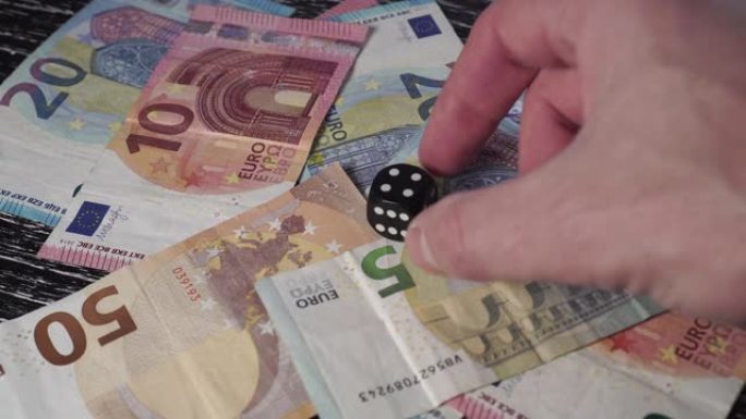在一堆欧元纸币上，一只手在上面放了一个数字4的黑色骰子