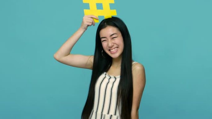 可爱的快乐亚洲女人，留着长长的黑发，拿着黄色的标签符号，跟随互联网趋势的哈希标志