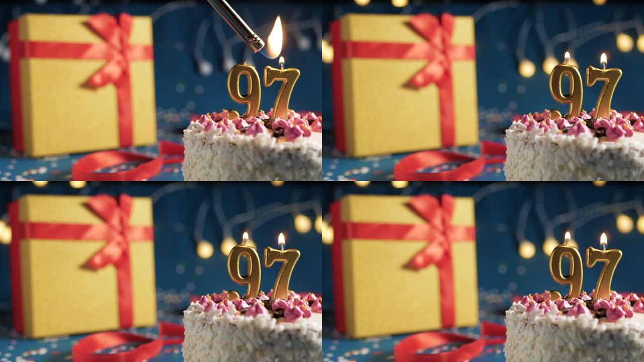 白色生日蛋糕97号点火器燃烧的金色蜡烛，蓝色背景带灯和用红丝带绑起来的礼物黄色盒子。特写