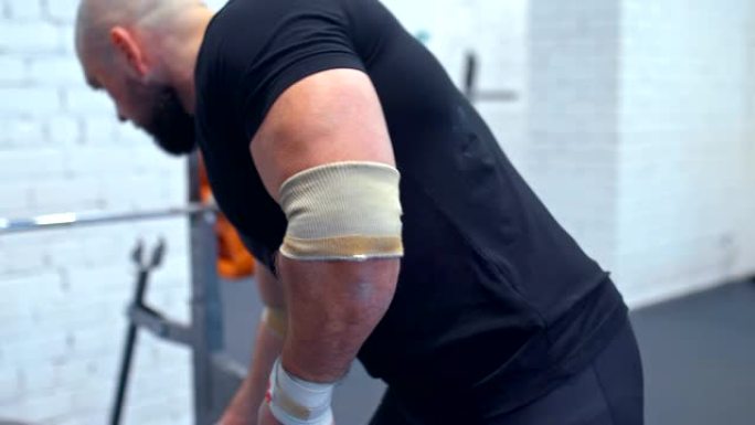 重量级男子用弹性绷带包裹手腕，为运动做准备。在健身房训练。特写。