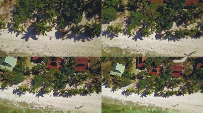 斐济金银岛，岛屿海滩上女孩挥舞着的4k天线躺在椰子和棕榈树周围的沙滩上。水晶般清澈的水和岩石浅水礁石