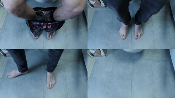 穿着牛仔裤的男性腿的特写镜头从厕所站起来。赤脚男子从浴室的白色厕所站起来，墙壁和地板上有灰色瓷砖