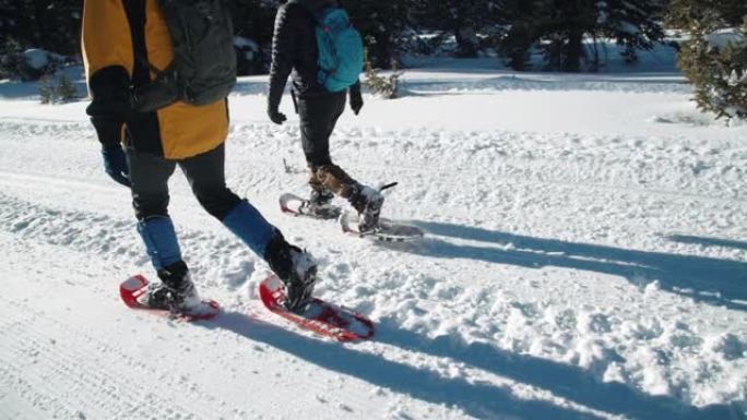 慢动作手持侧角跟随成年徒步旅行者从相机走到阳光下的拍摄雪鞋在户外深雪中行走