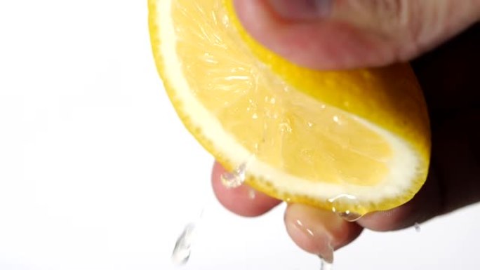 用手在白色背景上慢动作挤压新鲜柠檬。柠檬汁从果肉和滴水中排出。