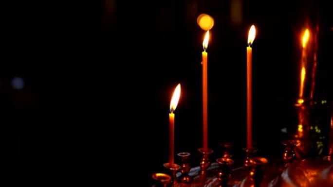 在黑暗背景下的教堂里，三支燃烧着的蜡烛插在一个金色的烛台上。