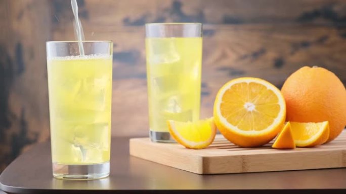用冰块将橙色碳酸柠檬水倒入玻璃杯中。在橙色水果的木制背景上