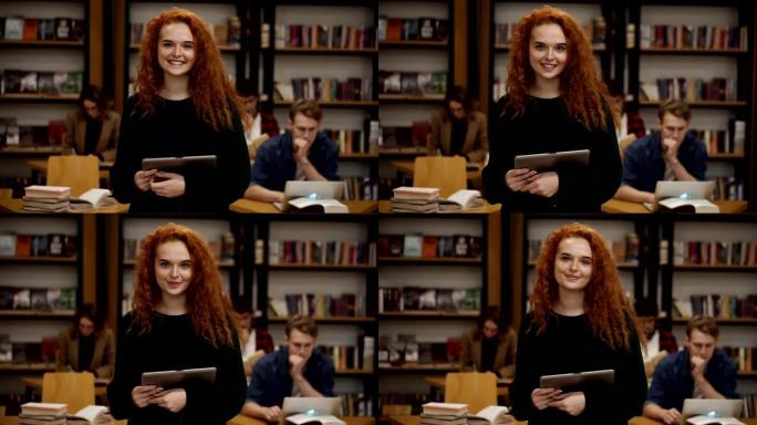 一位迷人的红发欧洲女学生站在高中图书馆的肖像，拿着平板电脑微笑着看着相机。教育、文学和人民观念。背景