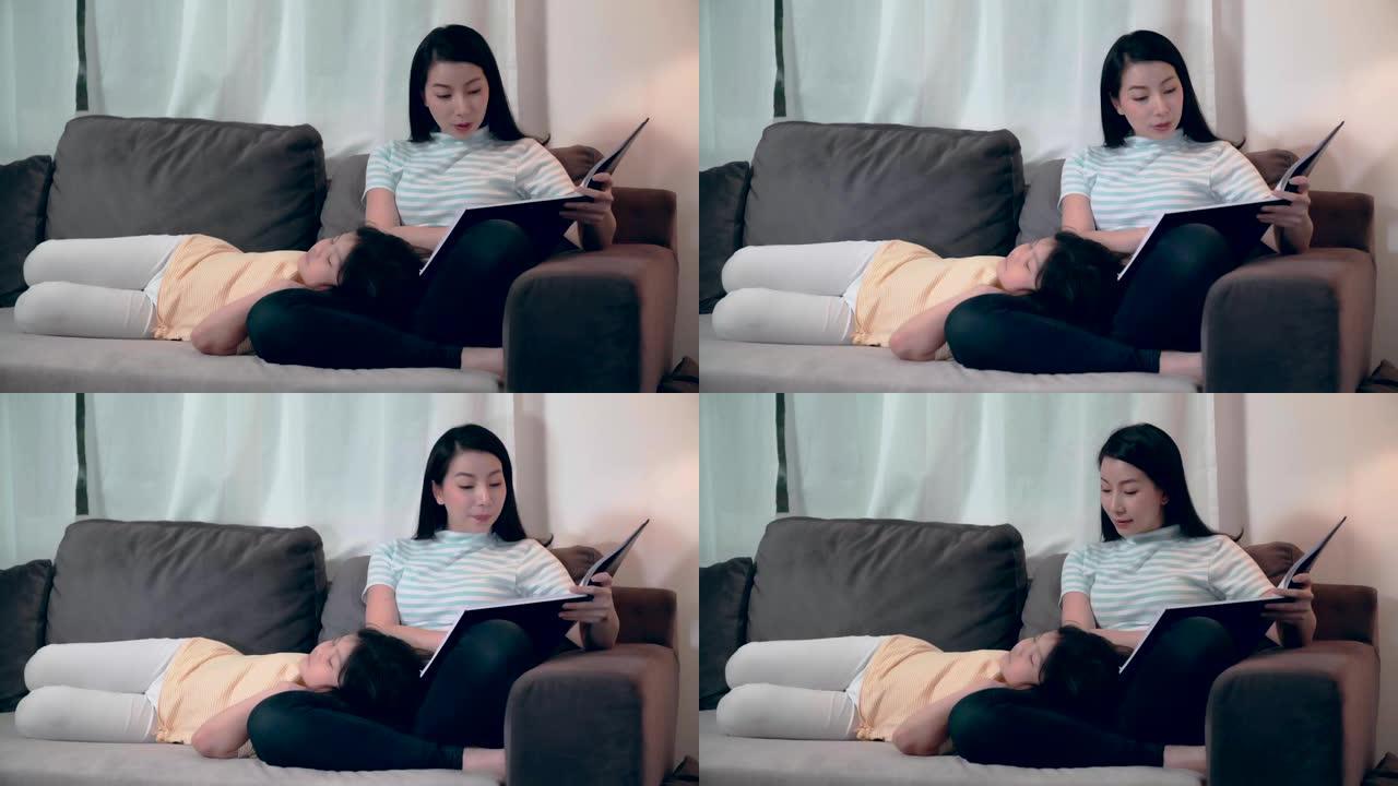 年轻迷人的亚洲妈妈在客厅夜间休闲活动中向沙发上漂亮可爱的女儿阅读儿童故事