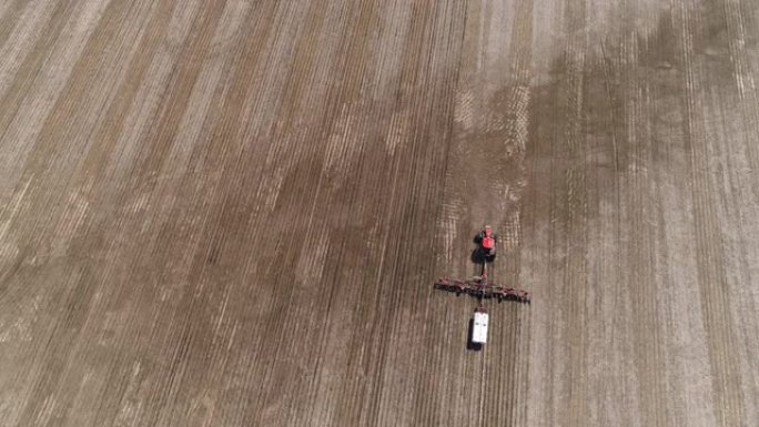 在美国伊利诺伊州林登镇附近的春季，拖拉机在农田上耕作和施肥。空中无人机视频，前摇摄摄像机在拖拉机后运