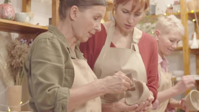 老年女士在陶器工作室制作粘土器皿，老师帮忙