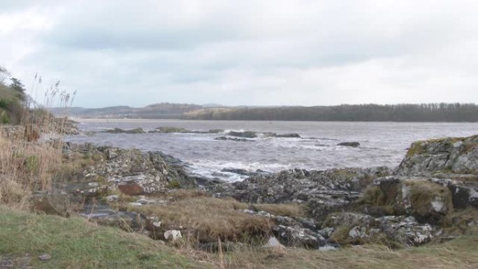 在苏格兰一个刮风的早晨，从岸上看淤泥海水冲刷在岩石上。