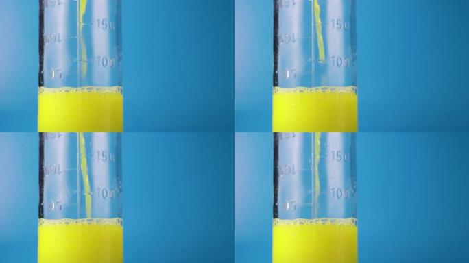 将黄色液体倒入玻璃杯中，在蓝色背景上测量烧瓶