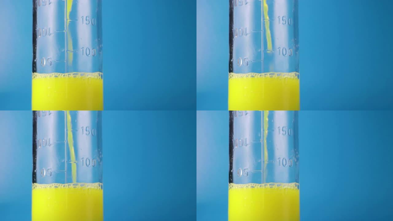 将黄色液体倒入玻璃杯中，在蓝色背景上测量烧瓶