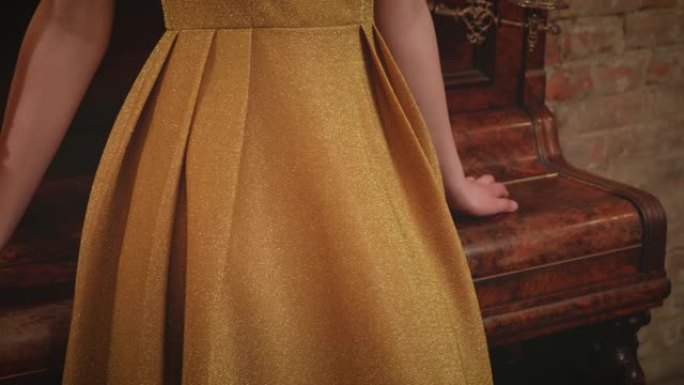 特写操作员脱下金色复古风格20年代优雅经典复古奢华连衣裙。美丽的女性手放在旧棕色钢琴上。背景是砖墙。