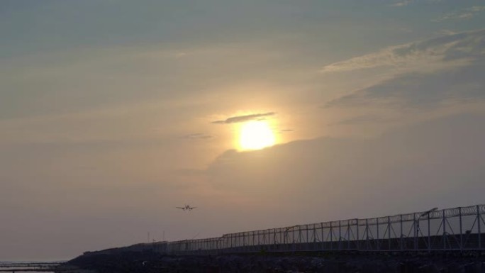 民用飞机在黄色的日落下降落在热带海滩附近的跑道上，太阳在后面