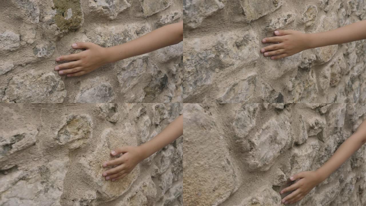 年轻的手触摸室外旧石墙。在步行时，近距离接触老街上石质墙面的青少年手。