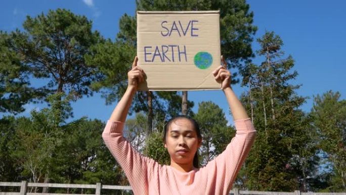 年轻女子举着 “拯救地球” 海报，上面写着抗议森林中塑料污染的标语。世界环境日的概念。零浪费。